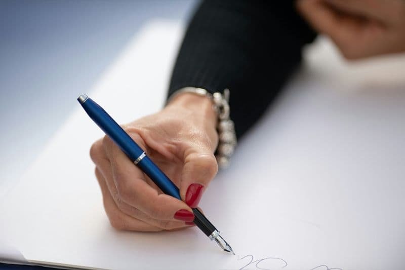 Hand signing financial documents with a fountain pen, representing strict adherence to U.S. GAAP and IRS tax regulations.